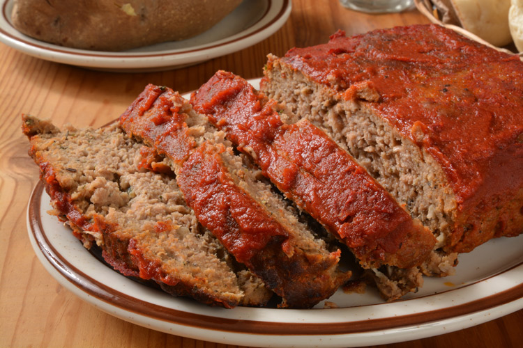 A piece of meatloaf and some meatloaf slices with tomato sauce.