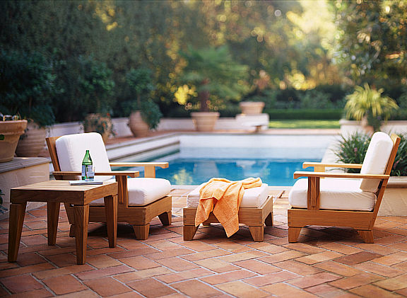 Patio furniture by the side of a swimming pool.