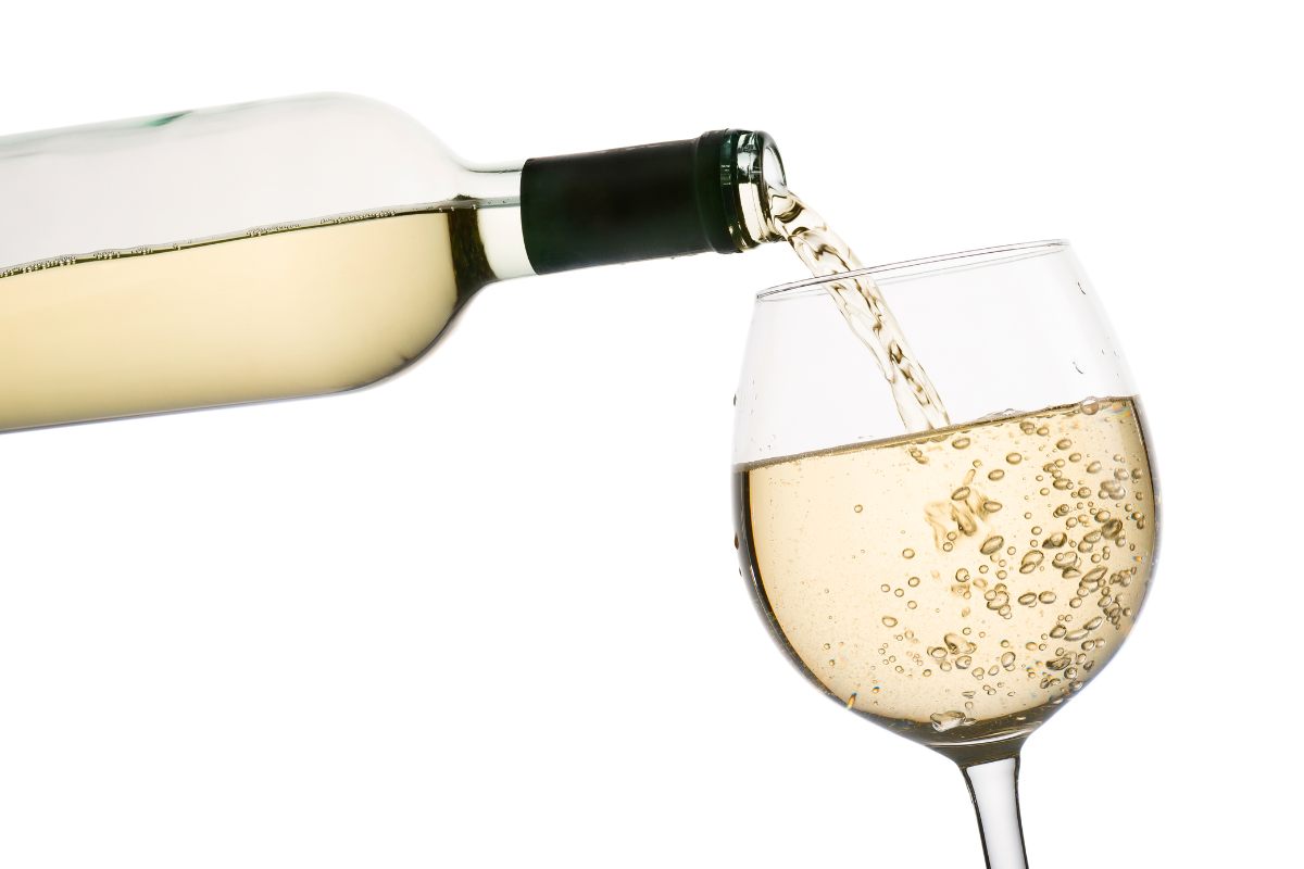 A bottle pouring white wine into a wine glass.