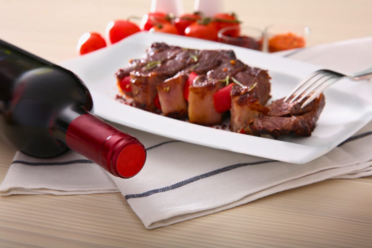 A serving plate with roast pork steak with a bottle of red wine by the side.