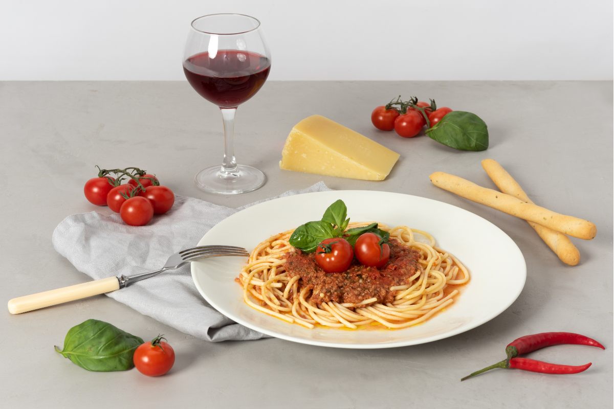 A plate of pasta Bolognese, cherry tomatoes, a glass or red wine and a piece of cheese.