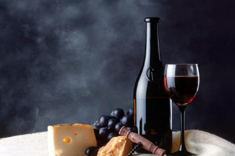 A bottle and a glass of red wine, cheese and grapes on a table.
