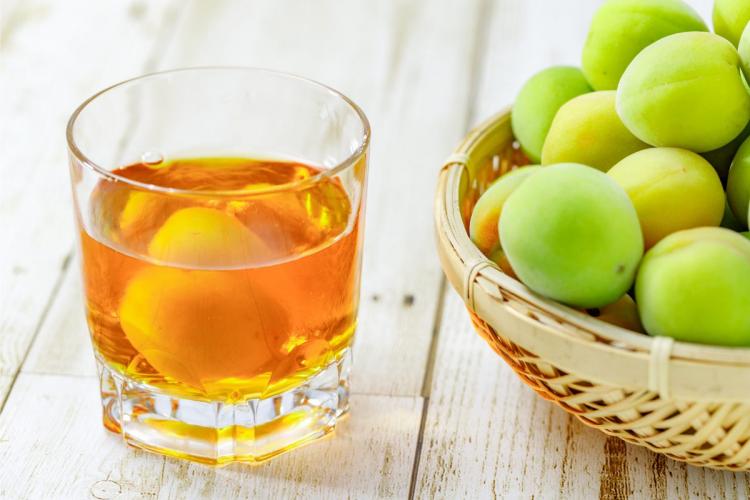 A glass of plum wine with a basket of fresh plums on the side.