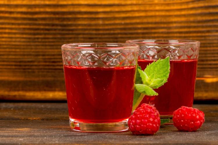 Two glasses with raspberry wine, two fresh raspberries and mint leaves.