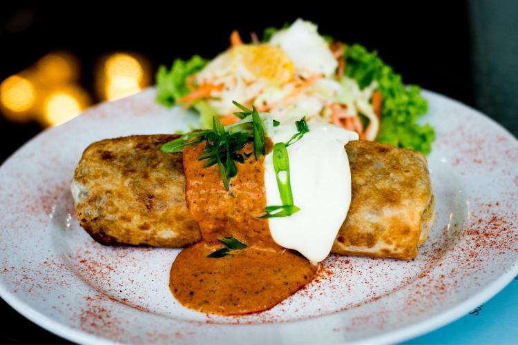 Oven baked chicken chimichanga topped with salsa and sour cream, served with a side salad.