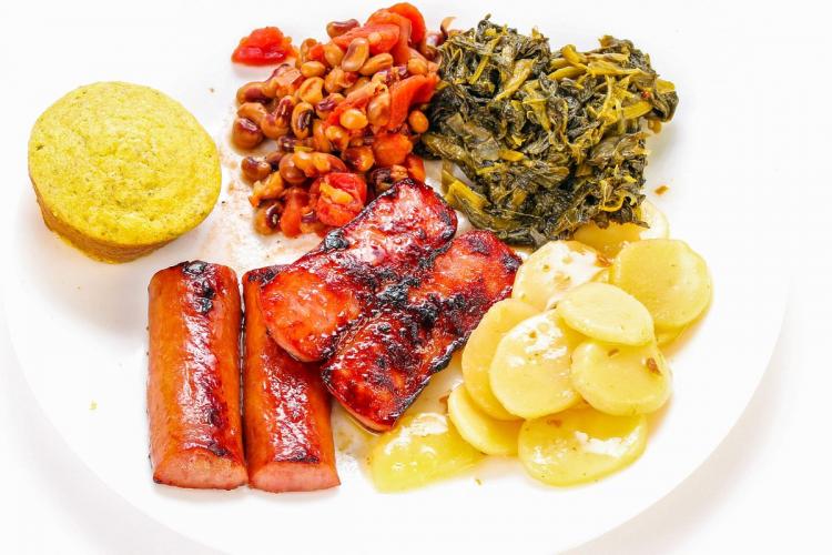 A plate with sausages, poatoes, collard greens, peas and corn muffin.