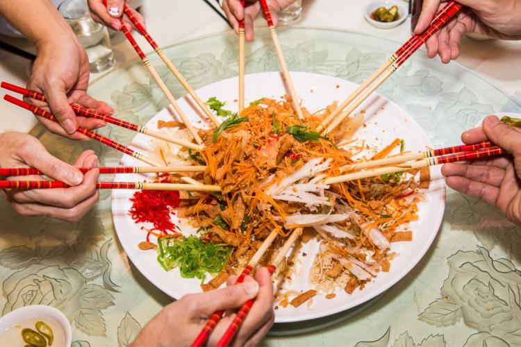 Yee sang salad on a serving plate with several hands around.