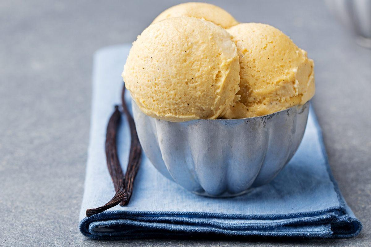 Three scoops of vanilla ice cream on a metal bowl and tow vanilla pods on the left side.