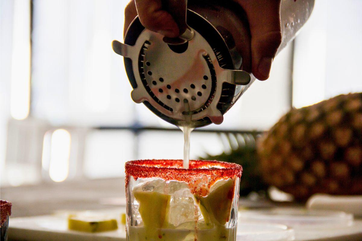 Pouring a cocktail from a shaker into a prepared glass.