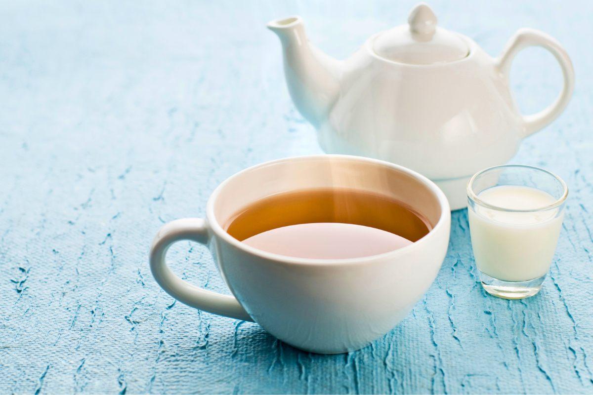 A cup of tea with tea pot and a little milk in a glass.