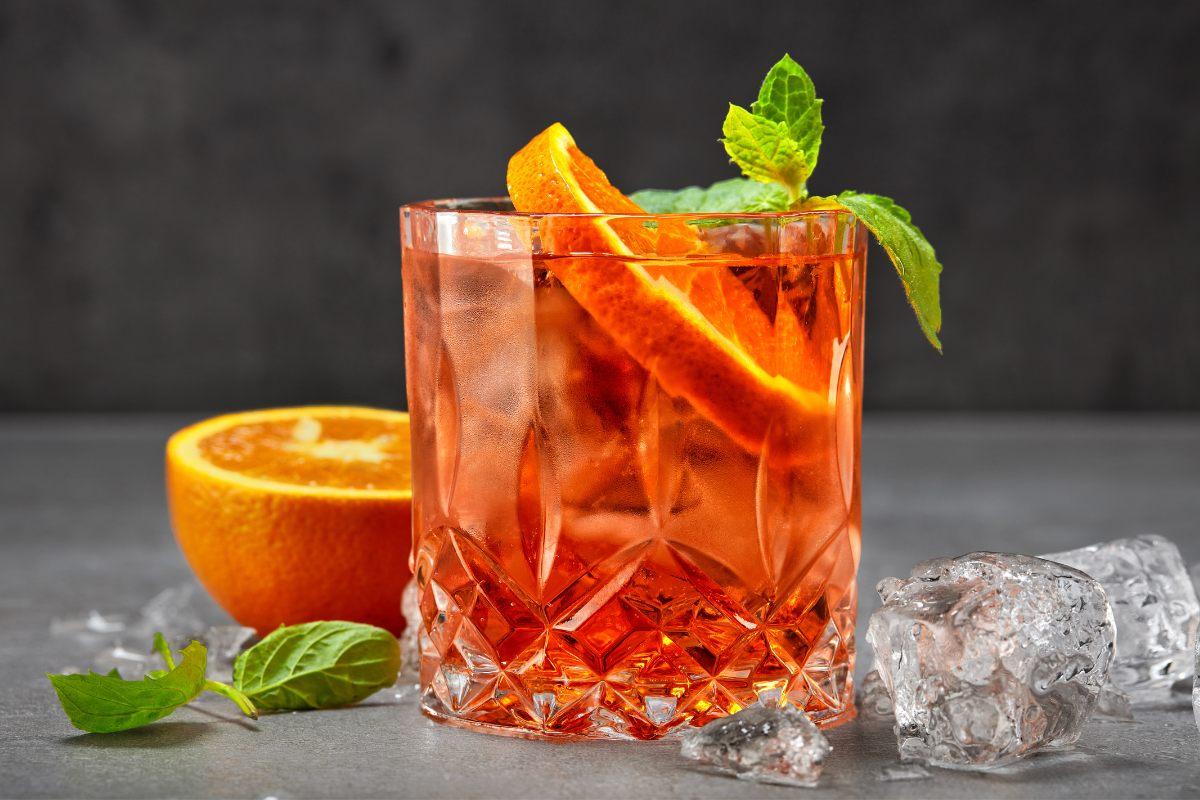 Aperol spritz in a crystal glass with orange slices and mint on a grey surface.