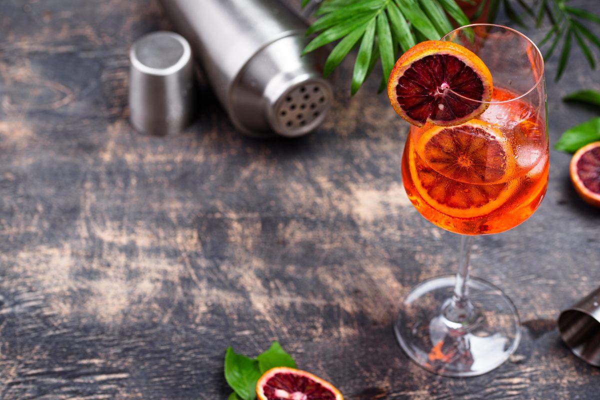 Blood orange spritz with slices of blood orange on a rustic surface with a shaker and jigger in the background.