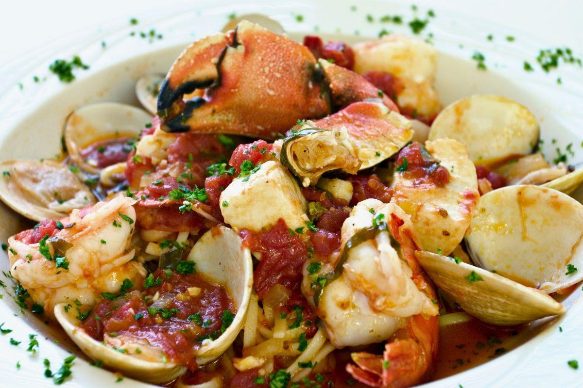 A bowl of cioppino seafood stew with shrimp, clams, and a large crab claw in a tomato-based broth, garnished with fresh parsley.