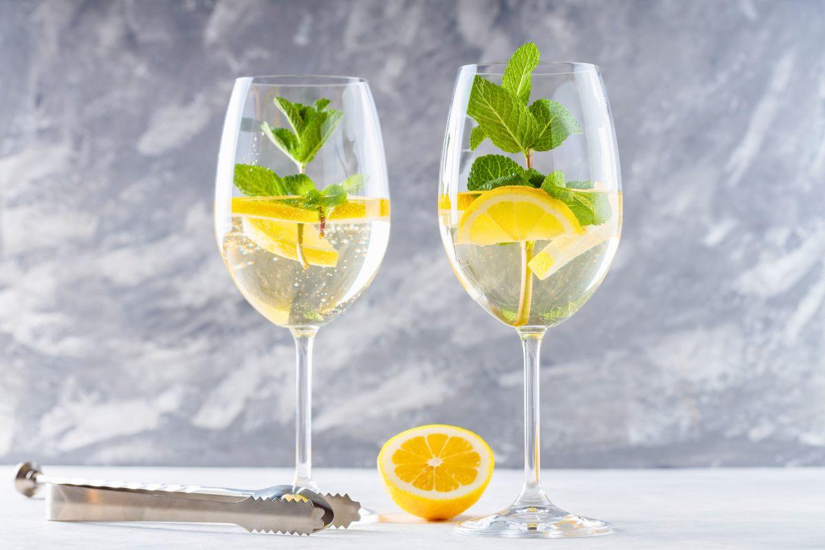 Two glasses of elderflower spritz with lemon slices and mint leaves on a light background.