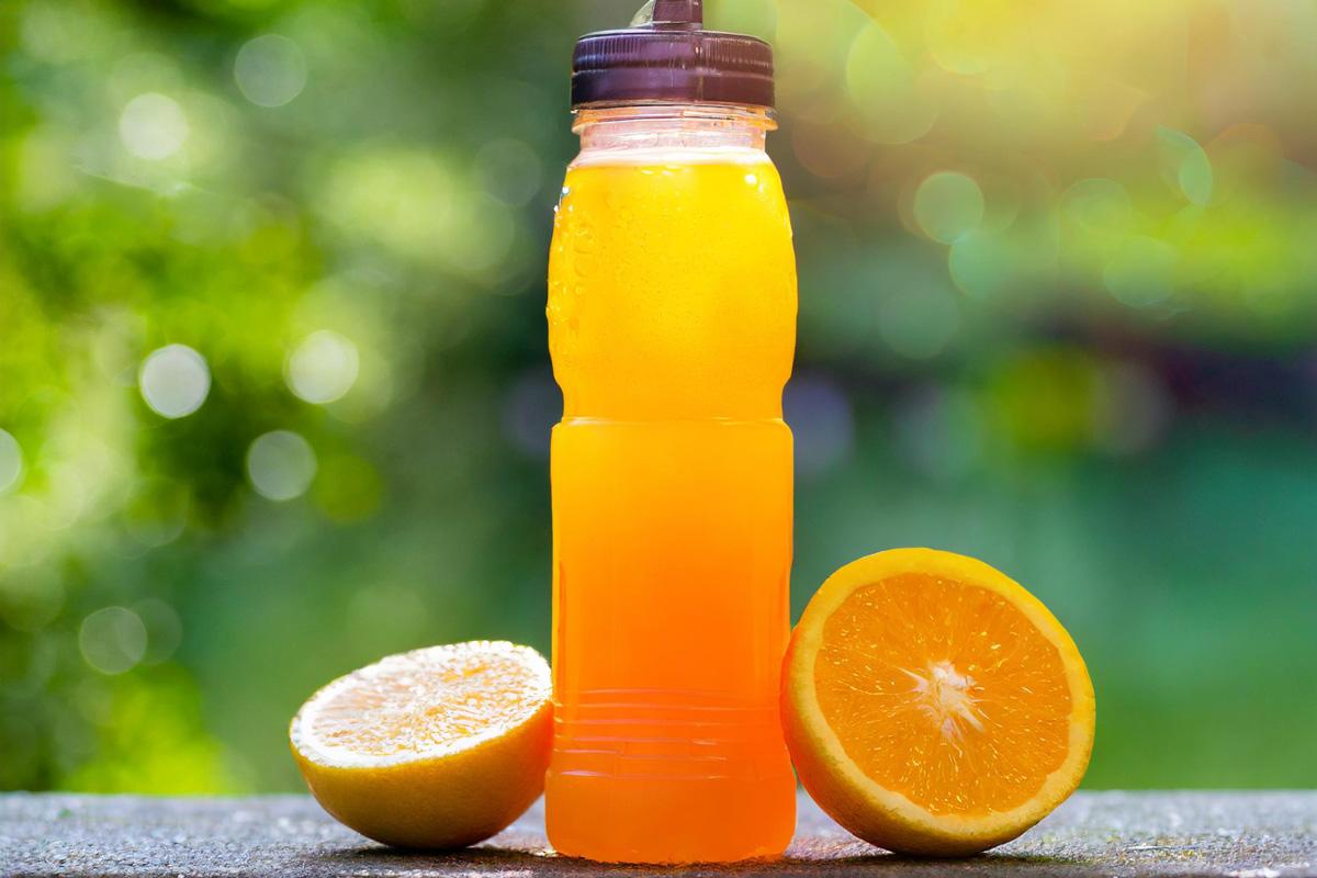 Cold orange drink with condensation. Orange halves. Outdoors. Green background.󠁧󠁢󠁳󠁣󠁴󠁿