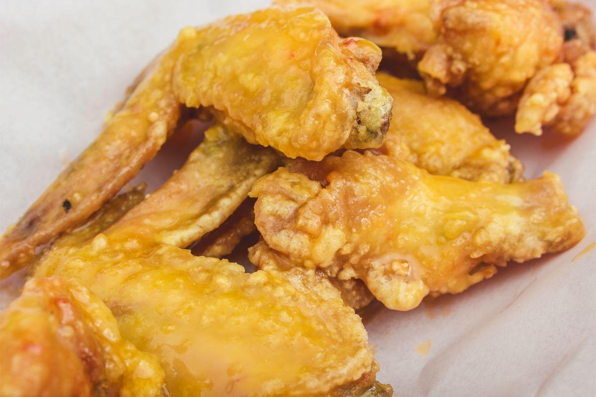 Close-up of crispy chicken wings coated with a glossy citrus glaze, showcasing a golden-brown crust and a sticky yellow-orange finish.