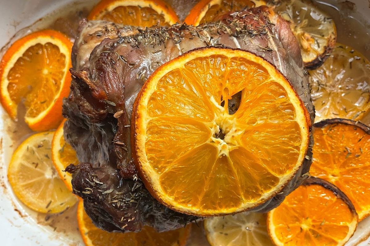 Slow-roasted lamb with thyme, fresh orange and lemon slices in a white baking dish, St Clement’s roast lamb dish with citrus and herbs.