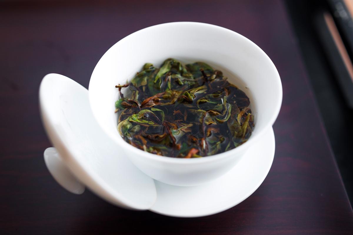 White porcelain gaiwan with steeping tea leaves in hot water, lid resting on the side.