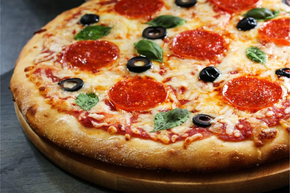 Detail of a homemade pepperoni pizza with black olives and fresh basil.
