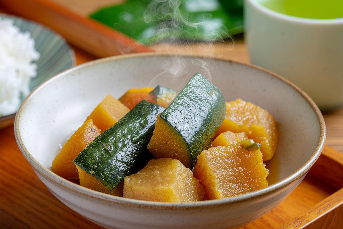 Homemade simmered kabocha squash in Japanese style, tender squash pieces in a light savory broth glaze, simple ceramic bowl, warm natural daylight, minimalist Japanese home kitchen aesthetic.