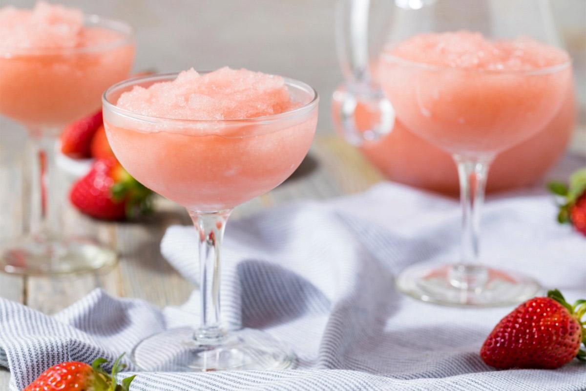 Pink semi-frozen Frosé cocktails in coupe glasses with fresh strawberries on a light cloth-covered table.