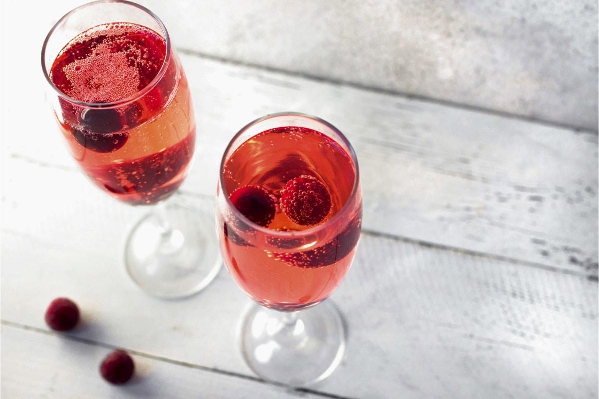 Two sparkling Kir Royale cocktails in stemmed glasses with floating berries on a white wooden table.