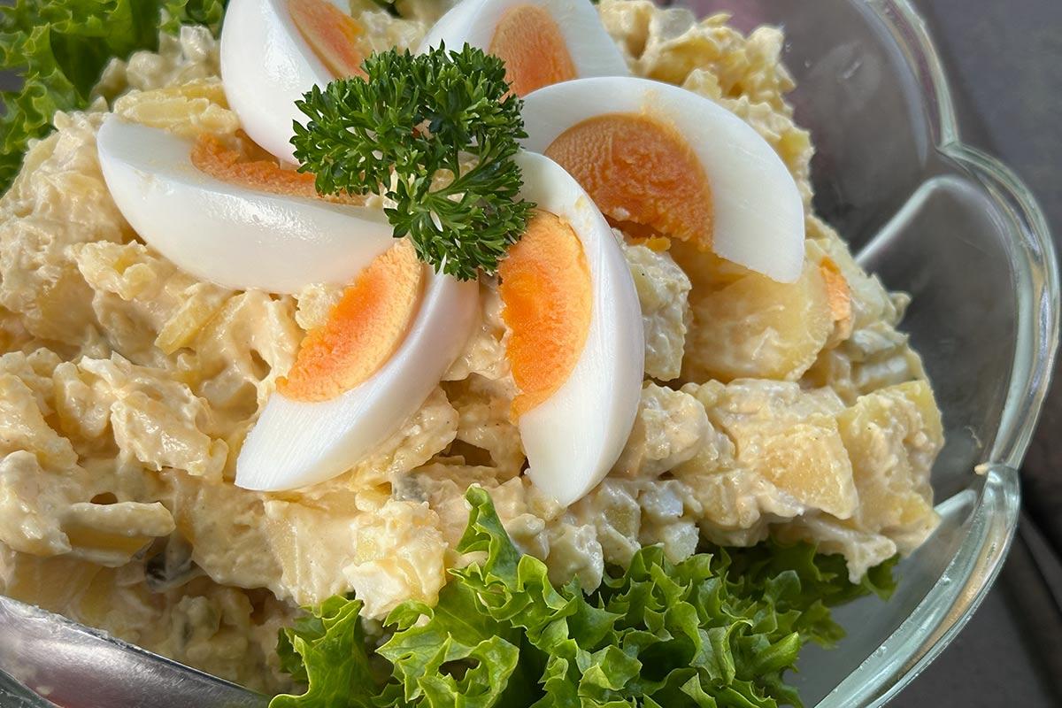 Creamy Northern German potato salad with mayonnaise dressing, topped with quartered hard-boiled eggs and fresh parsley, served on a bed of lettuce in a glass bowl.