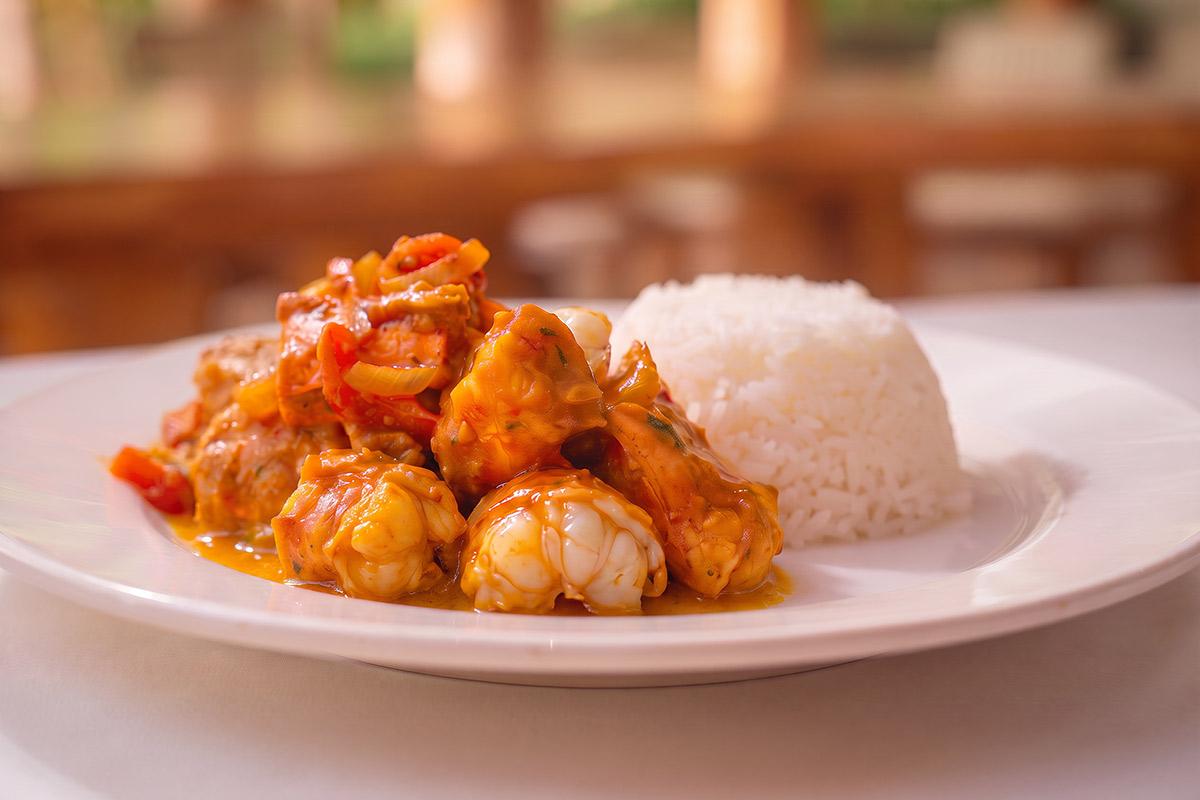 Chunks of lobster tail in a thick orange curry sauce with onion and red pepper, served beside a moulded dome of white rice on a white plate