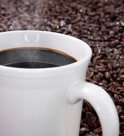 A cup with dark coffee with a background of roasted coffee beans.