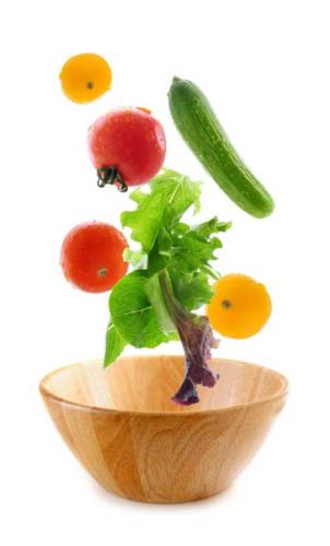 Salad ingredients falling into a wooden salad bowl.