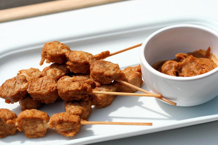 Three chicken satays with a bowl of peanut sauce.