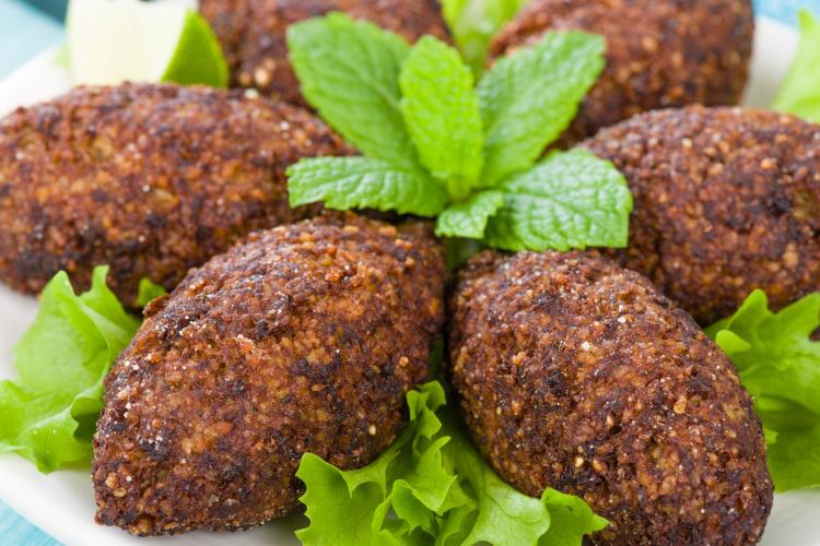 Plate of elongated, fried kibbeh garnished with fresh mint leaves and surrounded by lettuce leaves.