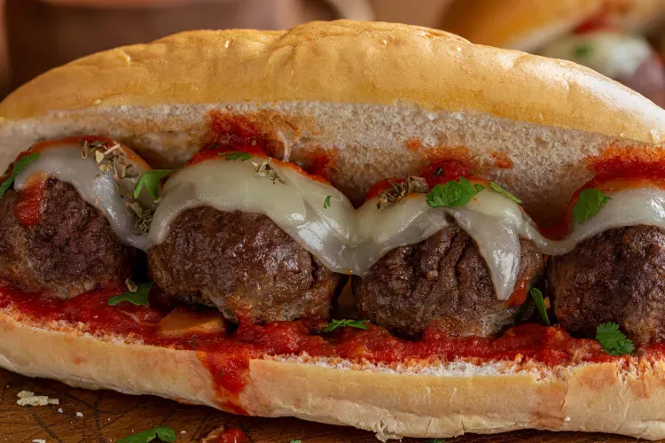 Close-up of a meatball hoagie sandwich with large meatballs topped with melted provolone cheese, garnished with parsley and dried herbs, in a soft hoagie roll with marinara sauce.