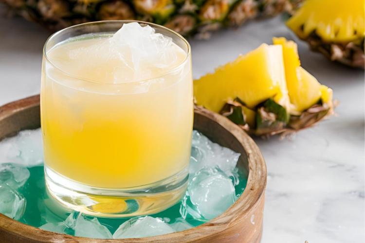 Pineapple coconut spritz with ice in a glass, surrounded by pieces of fresh pineapple.