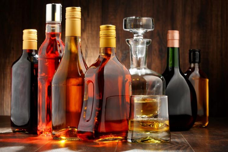 An assortment of spirit bottles in various shapes and colors on a wooden surface, with a glass of whiskey and a decanter.