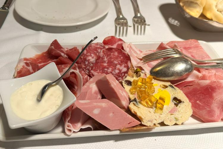 Plate of assorted Emilia-Romagna cured meats with prosciutto, salami, mortadella, terrine garnished with jelly cubes, and a side of squacquerone cheese.