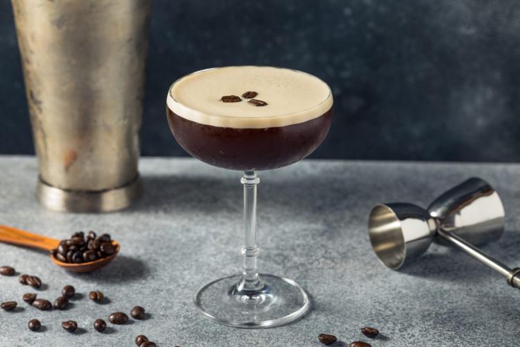 Espresso Martini cocktail in a coupe glass with a creamy foam top, garnished with three coffee beans, surrounded by coffee beans and bar tools