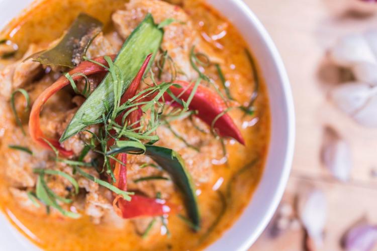 A bowl of panang chicken curry with red chilies, makrut lime leaves, and herbs in a rich orange sauce.