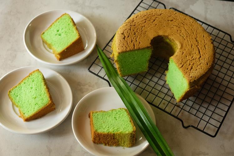 A pandan chiffon cake, with a piece cut out, resting on a grid support with three slices on serving plates in front.