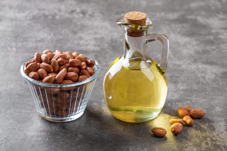 Bottle of peanut oil with cork next to a bowl of peanuts on a gray countertop.