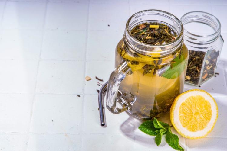A jar with cold brewed tea with half a lemon and some tea leaves by the side.