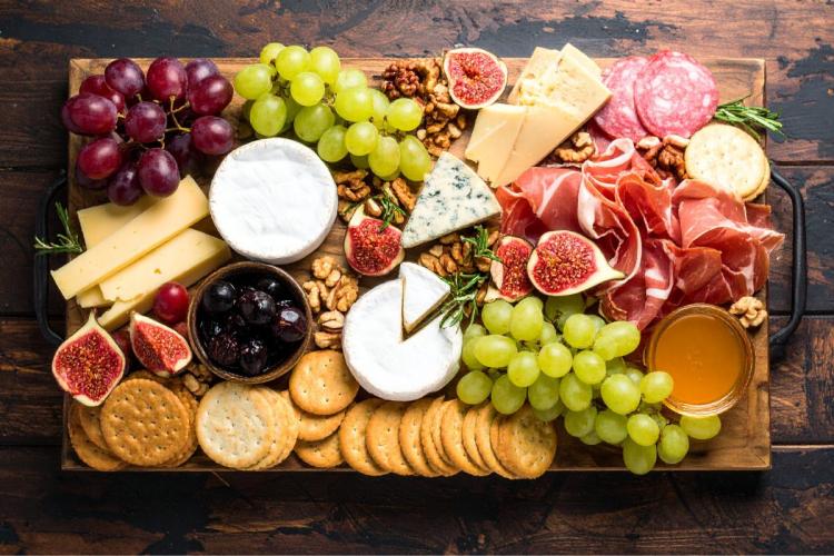 Charcuterie board with assorted cheeses, cured meats, grapes, figs, nuts, olives, and crackers on a wooden serving board.