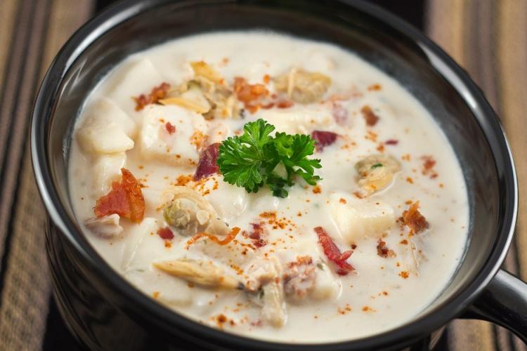 Bowl of New England clam chowder with potatoes, clams, and bacon, garnished with parsley.