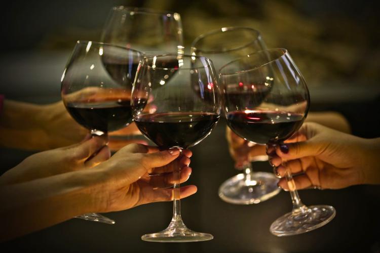 Four people share a toast and clink wine glasses filled with red wine.