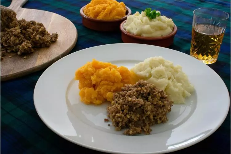 Plate of haggis, mashed rutabaga, or neeps, and mashed potatoes or tatties on tartan cloth.
