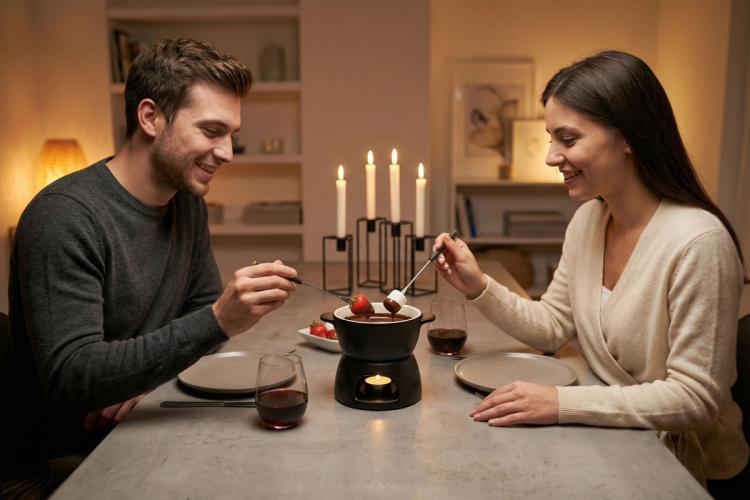 wo people dip strawberries and marshmallows into a chocolate fondue pot by candlelight.