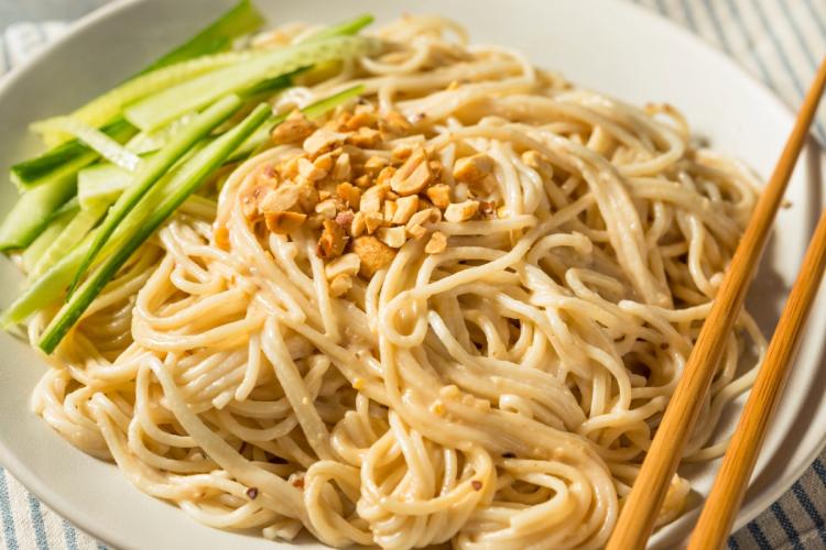 A shallow bowl of cold sesame noodles garnished with cucumber.