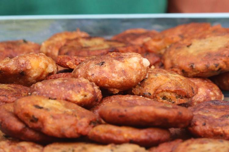 Close-up of a tray of golden-brown fried potato patties stacked together, with one broken open to show the soft filling inside.