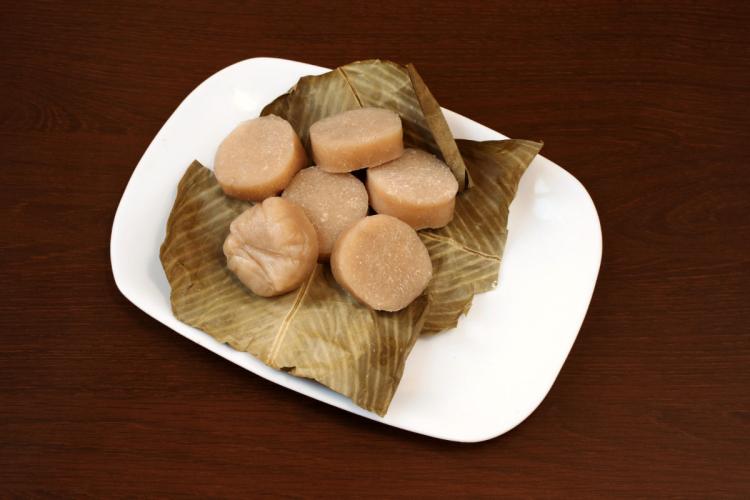 Pieces of chikwangue on banana leaves served on a white plate.