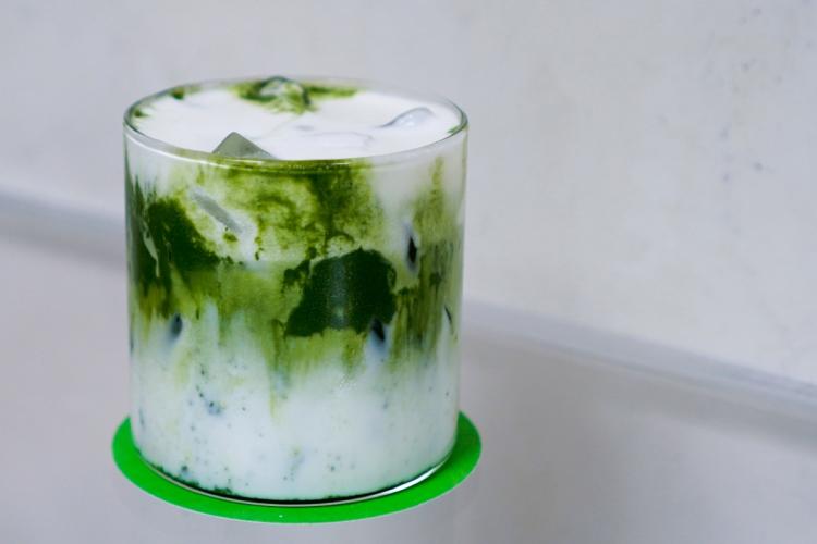 Glass of iced matcha Einspänner with green matcha swirls, milk, and ice cubes on a green coaster against a minimalist light background.